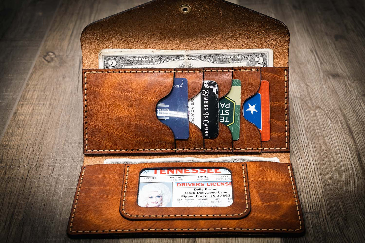 Women's leather wallet clutch in chestnut brown, handmade in the USA, displayed on a wooden surface with a rustic metal tool in the background.