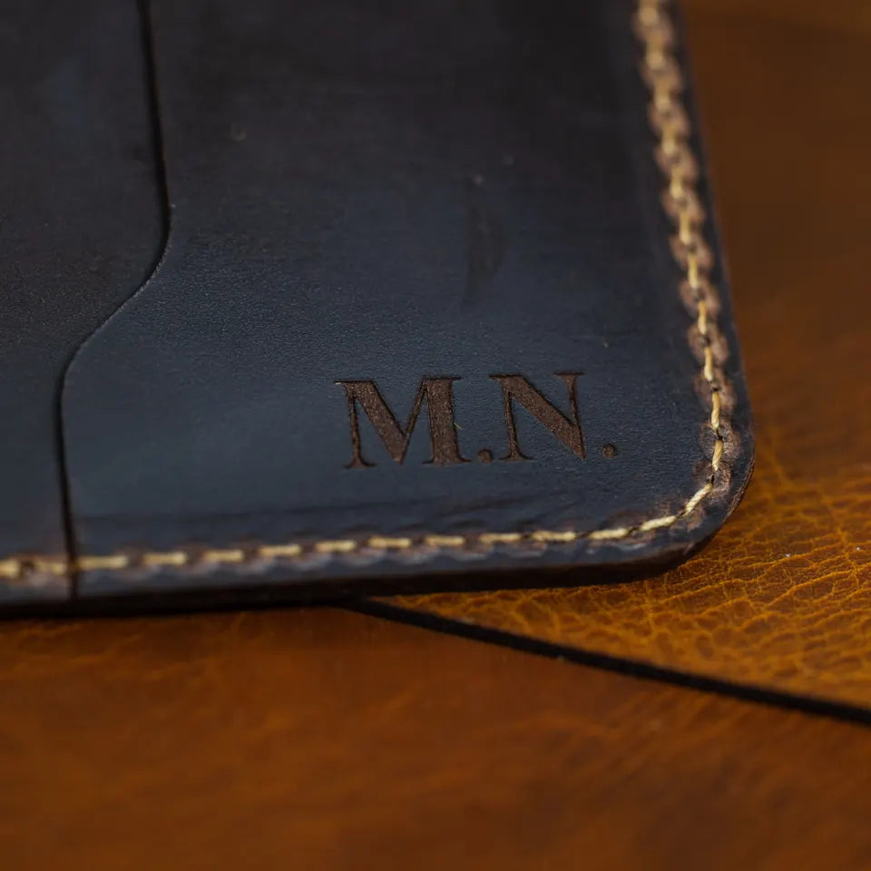 Close-up of black leather wallet with the initials M.N. engraved in a serif font beside the stitched edge