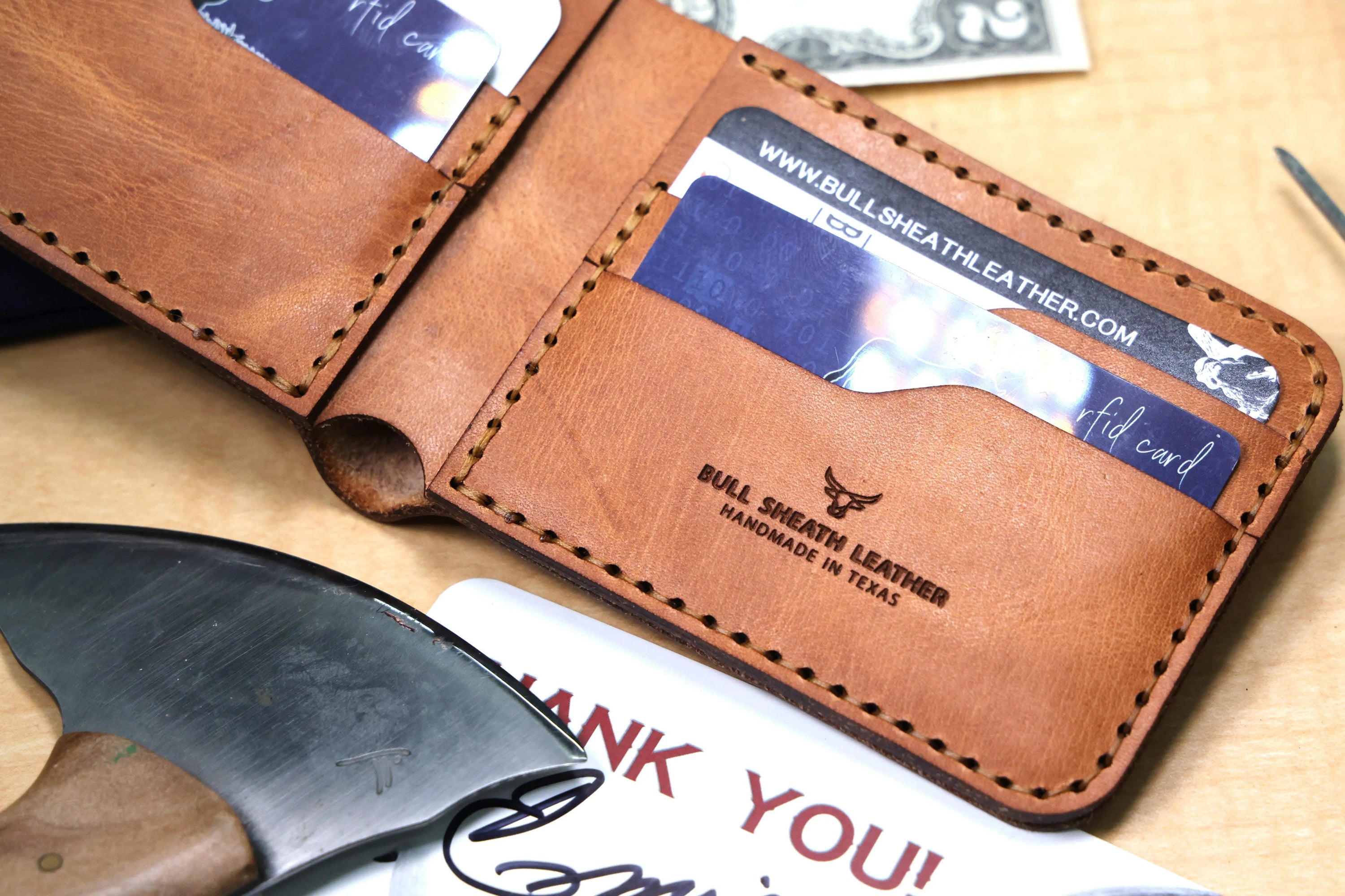 A handcrafted, saddle tan, leather bifold wallet open with leather crafting tools nearby.
