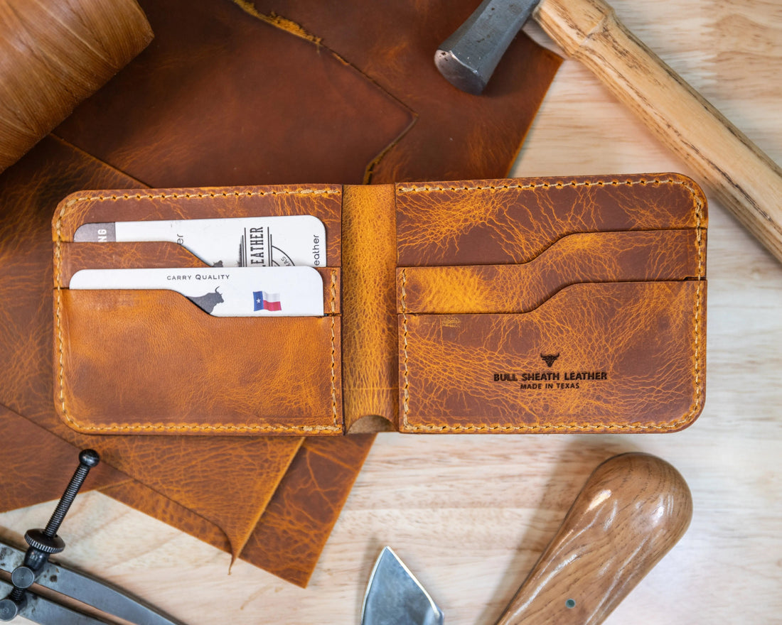 Handcrafted brown leather bifold wallet open on a wooden surface, holding business cards and surrounded by leatherworking tools.