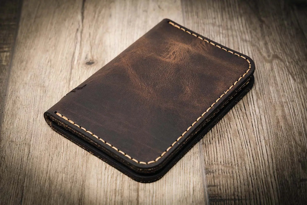 Handmade walnut brown leather wallet with vertical minimalist design, featuring beige stitching, on a wooden surface.