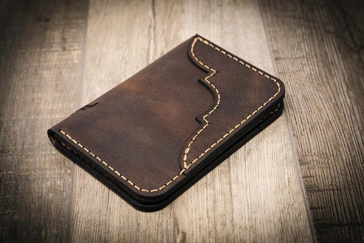 Handmade walnut brown leather wallet with vertical minimalist design, featuring beige stitching, on a wooden surface.