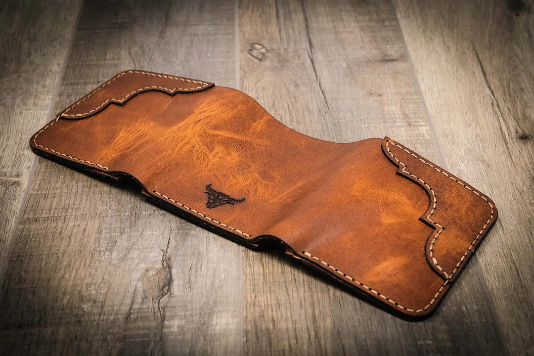 Trinity western trifold wallet in chestnut brown leather, featuring intricate stitching and a subtle embossed logo, displayed open, facedown on a wooden surface.