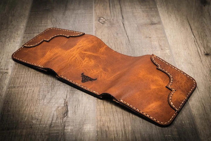 Trinity western trifold wallet in chestnut brown leather, featuring intricate stitching and a subtle embossed logo, displayed open, facedown on a wooden surface.