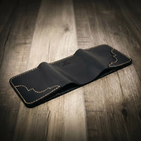 Trinity western trifold wallet in chestnut brown leather, featuring intricate stitching and a subtle embossed logo, displayed open, facedown on a wooden surface.
