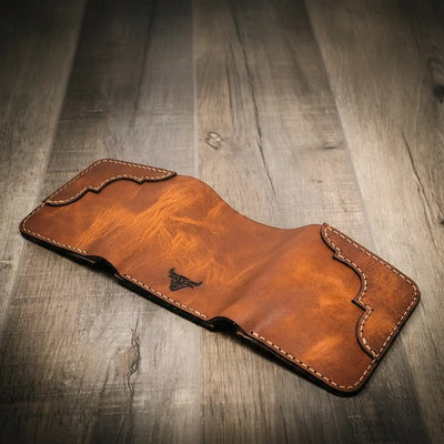 Trinity western trifold wallet in chestnut brown leather, featuring intricate stitching and a subtle embossed logo, displayed open, facedown on a wooden surface.
