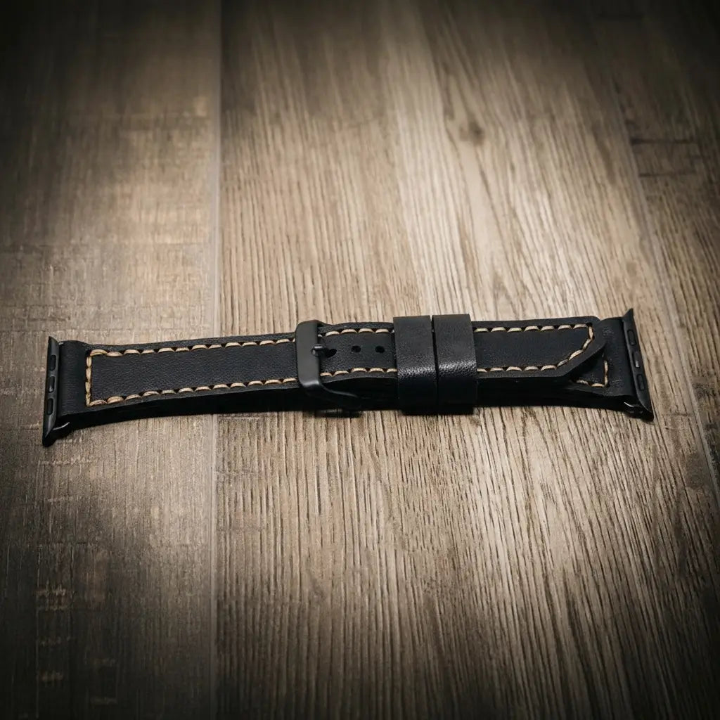 Apple Watch Leather Band in black full-grain leather with tan stitching on wood floor.