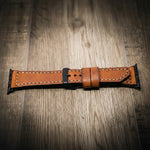 Brown full-grain leather Apple Watch band with black buckle and contrast stitching on wood surface.