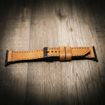 Light tan full-grain leather Apple Watch band with black buckle and stitched edges on wood surface.