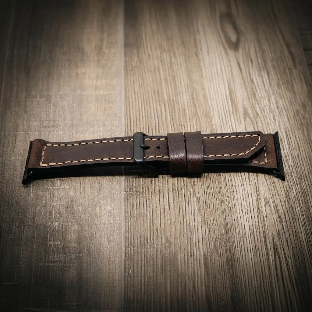 Brown full-grain leather Apple Watch band with tan stitching and black buckle on wooden surface
