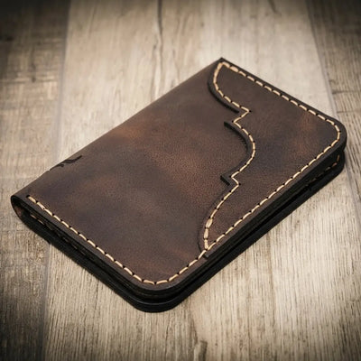 Handmade walnut brown leather wallet with vertical minimalist design, featuring beige stitching, on a wooden surface.
