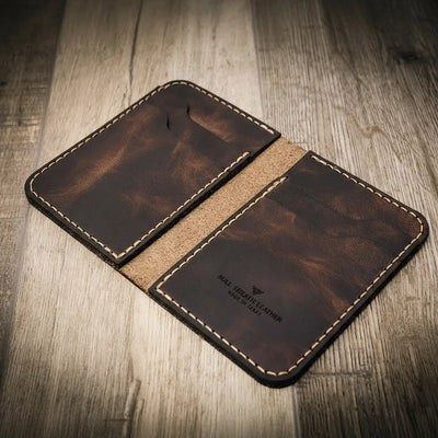 Handmade leather wallet in walnut brown color with visible stitching, branded "Bull Sheath Leather" and "Made in Texas," on a wooden surface.