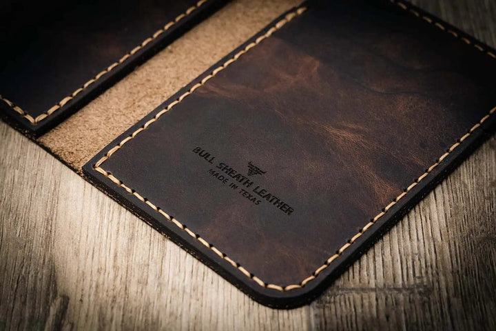 Handmade leather wallet in walnut brown color with visible stitching, branded "Bull Sheath Leather" and "Made in Texas," on a wooden surface.