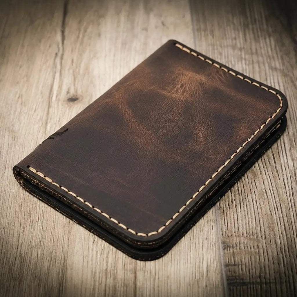 Handmade walnut brown leather wallet with vertical minimalist design, featuring beige stitching, on a wooden surface.