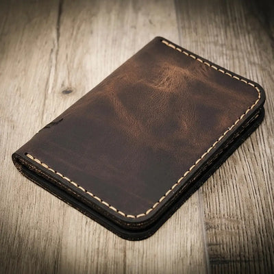 Handmade walnut brown leather wallet with vertical minimalist design, featuring beige stitching, on a wooden surface.