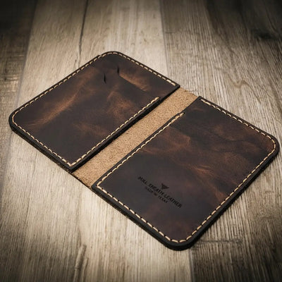 Handmade leather wallet in walnut brown color with visible stitching, branded "Bull Sheath Leather" and "Made in Texas," on a wooden surface.
