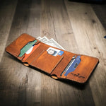 Trinity western trifold wallet in chestnut brown leather, featuring multiple card slots, a cash compartment, and a clear ID window, displayed open with cards and cash inside.
