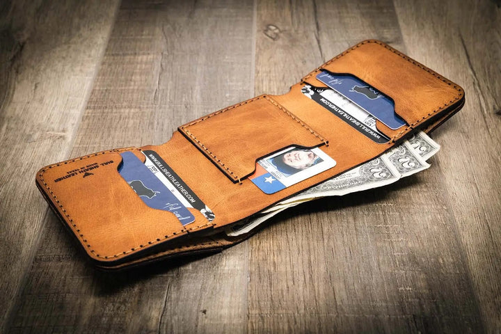 Trinity western trifold wallet in saddle tan leather, featuring multiple card slots and a cash compartment, displayed open on a wooden surface.