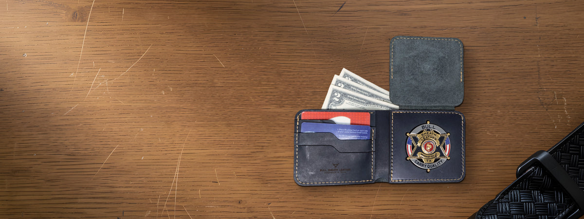 Black Badge Bifold Wallet open with a badge, cards and cash on an oak desk beside a black basket-weave duty belt and flashlight