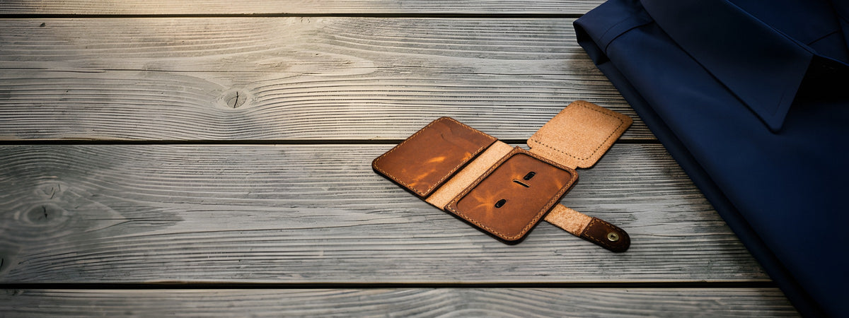 Badge Vertical Wallet in chestnut full-grain leather open on weathered grey barnwood beside a folded navy shirt