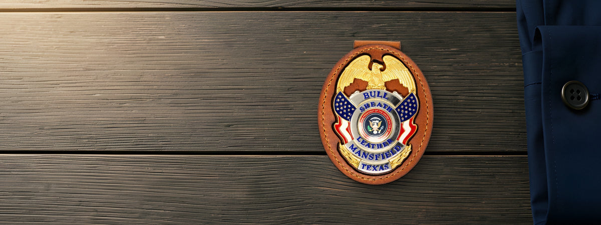 Belt Badge Holder in chestnut full-grain leather holding a demo badge on weathered grey barnwood beside a navy shirt