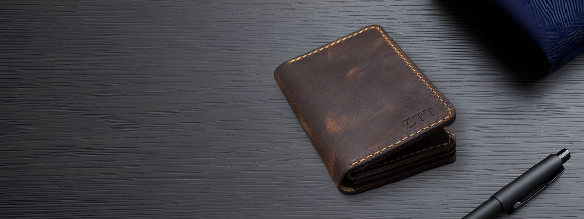 Federal Badge Wallet in dark brown full-grain leather closed on a dark wood desk beside a pen