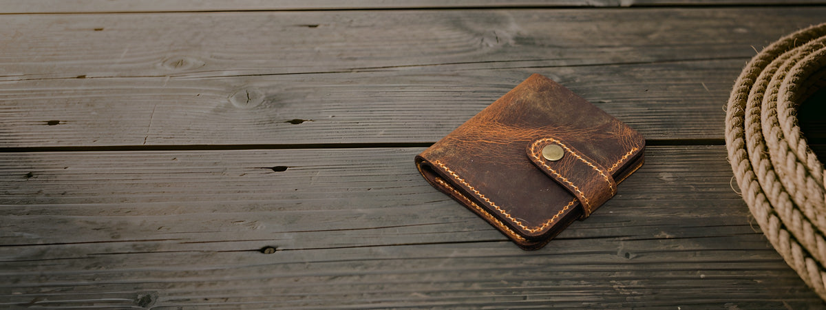 Glory Snap Bifold Wallet in brown full-grain leather closed on weathered barnwood beside a coiled rope
