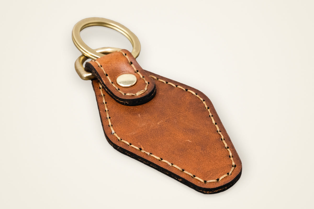 Leather Keychain on a cream background, showing its solid brass ring, horween full-grain leather, stitched edge, patina that grows with you
