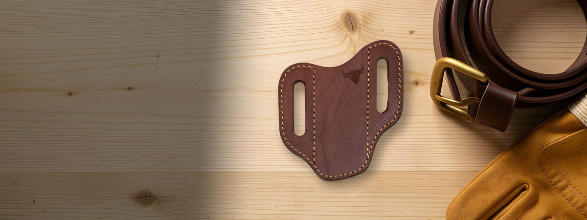Custom Leather Knife Sheath in brown full-grain leather on a light wood bench beside a leather belt and work gloves