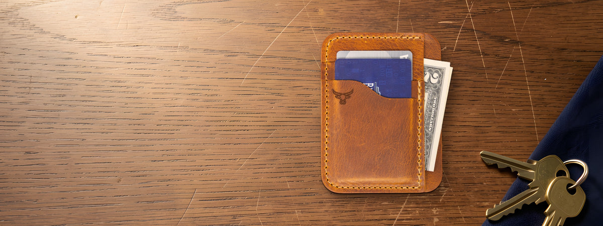 Mansfield Minimalist Wallet in chestnut full-grain leather with cards and cash on an oak table beside keys