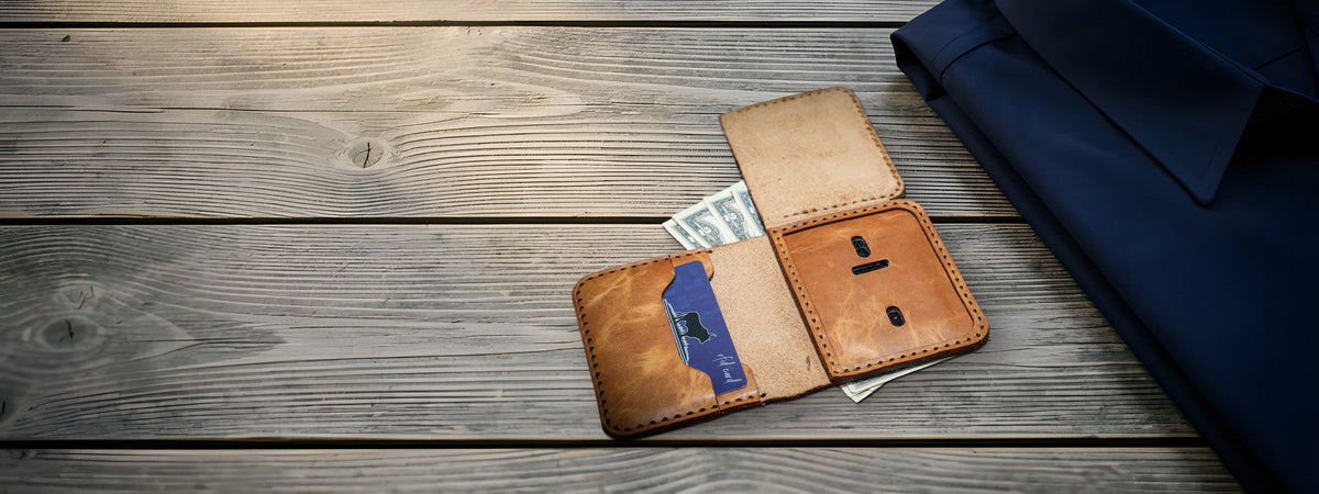 Minimalist Badge Wallet in chestnut full-grain leather open with cards and cash on weathered grey barnwood beside a navy shirt