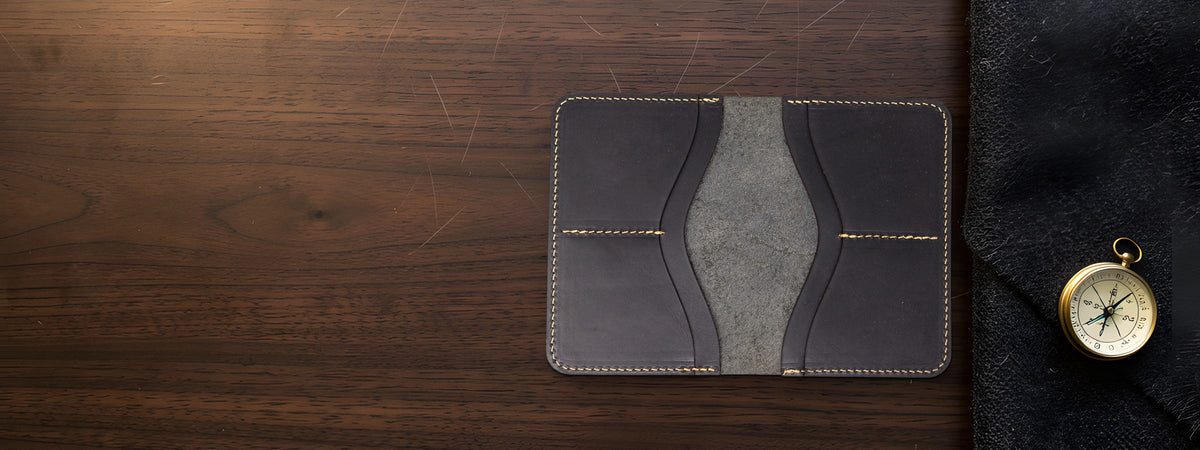 Nomad Leather Passport Holder in dark brown full-grain leather open on a dark walnut table beside a brass compass