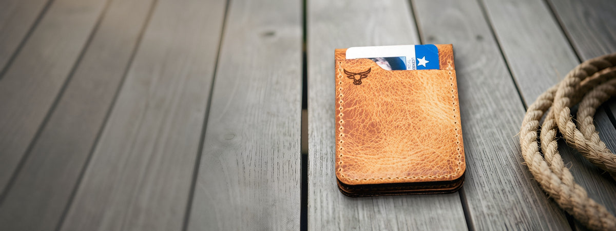 Peyton Small Card Holder in chestnut full-grain leather holding cards on weathered barnwood beside a coiled rope