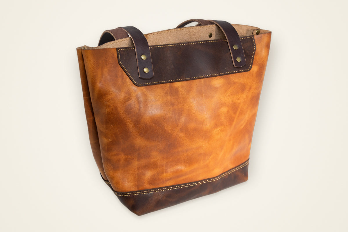 The Naomi Leather Tote Bag on a cream background, showing its top handles, room for your day, full-grain horween leather, stitched and edge-burnished