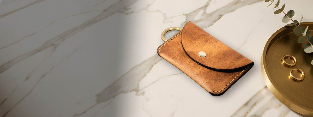 The Richmond wallet in chestnut full-grain leather closed on white marble beside a brass tray