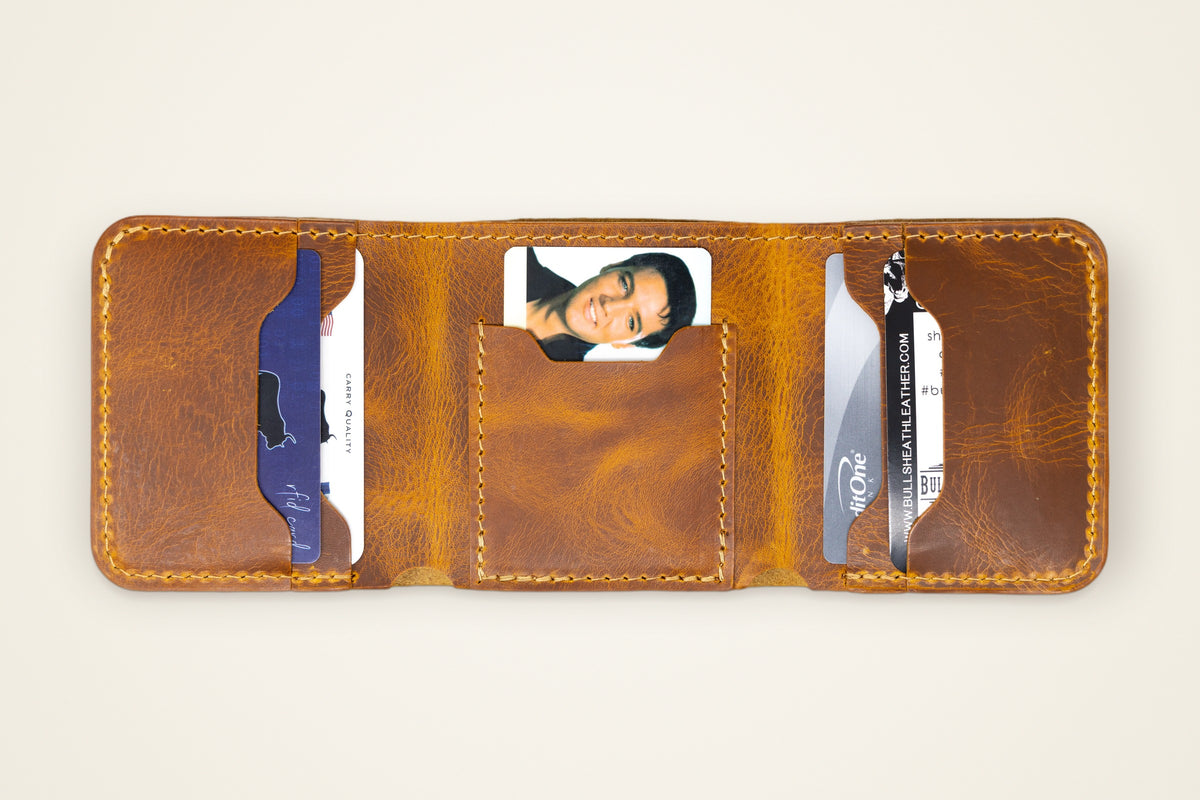 The Trinity Trifold Wallet on a cream background, showing its five card slots, room for 15+ cards, built for the fold, horween full-grain leather