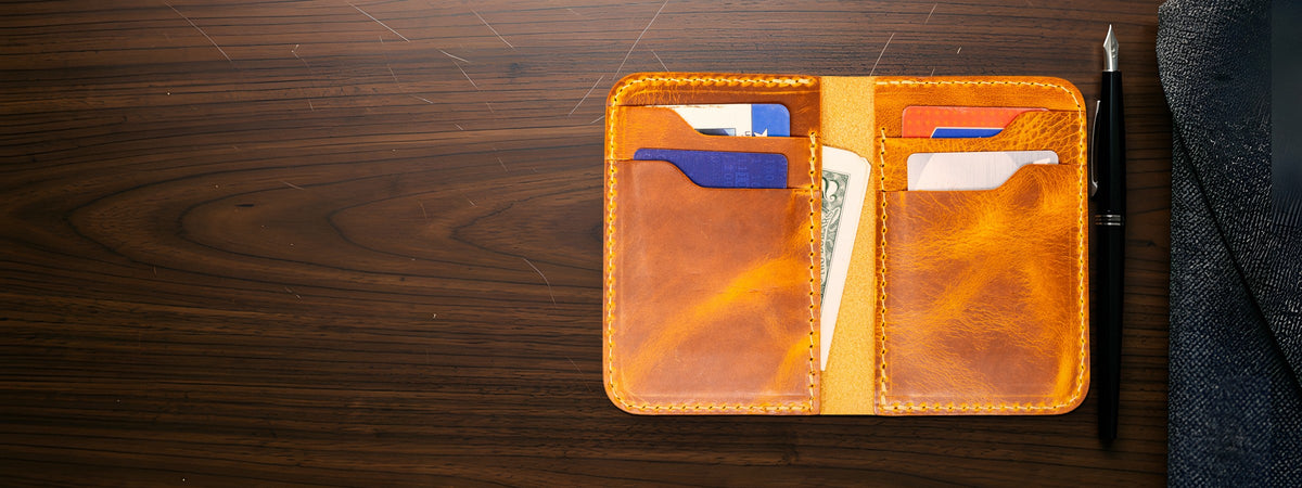 Tyler Vertical Wallet in chestnut full-grain leather open with cards and cash on a dark walnut table beside a pen