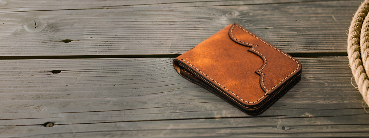 Western Bifold Wallet in brown full-grain leather closed on weathered grey barnwood beside a coiled rope