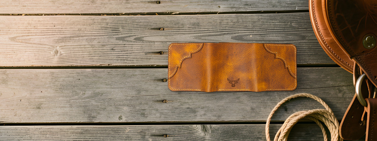 Western Trifold Wallet in chestnut full-grain leather closed on weathered barnwood beside a saddle and rope