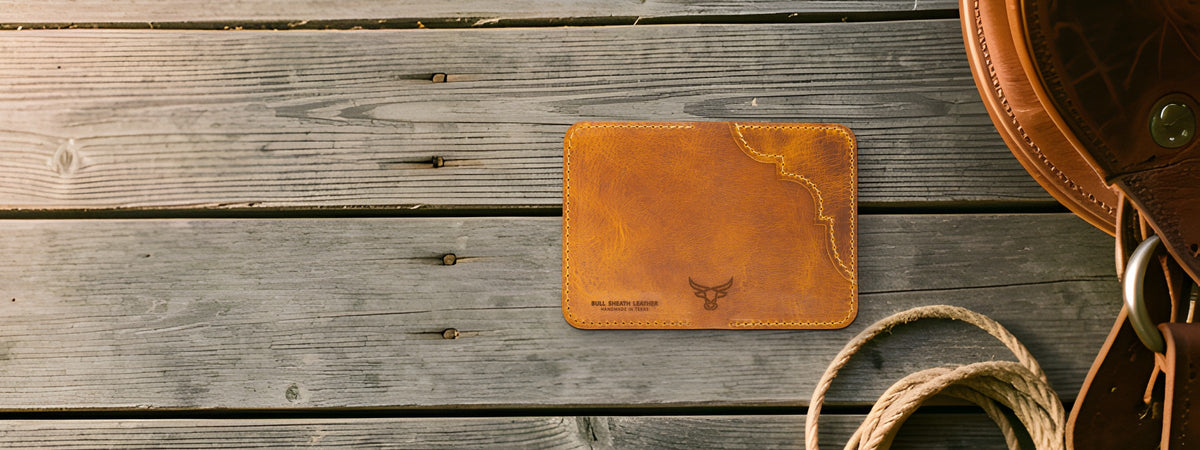 Western Vertical Wallet in chestnut full-grain leather closed on weathered barnwood beside a saddle and rope