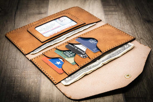Handmade women's long wallet in saddle tan leather, open to show card slots, ID window, and cash compartment, on a wooden surface.