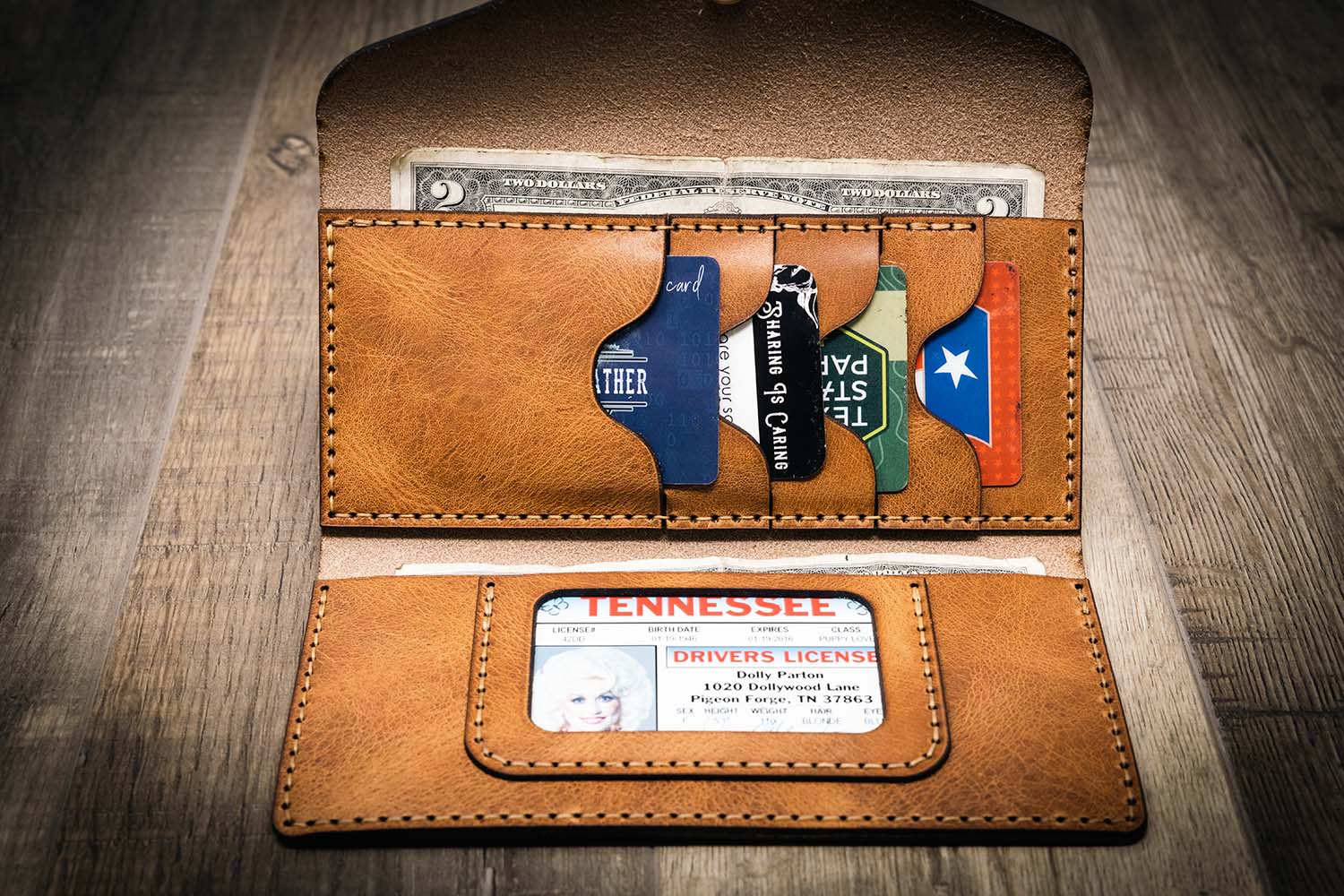 Handmade women's long wallet in saddle tan leather, featuring multiple card slots and an ID window, displayed open on a wooden surface.