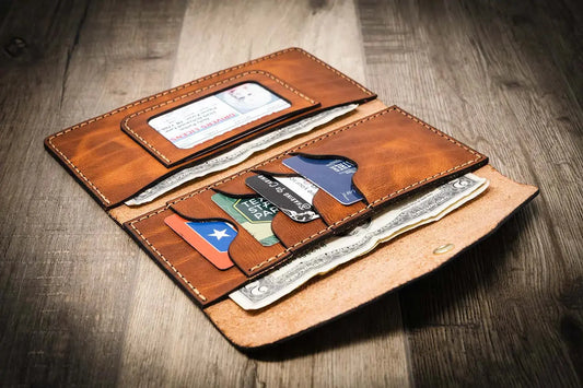 Women's leather wallet clutch in chestnut brown, handmade in the USA, displayed on a wooden surface with a rustic metal tool in the background.