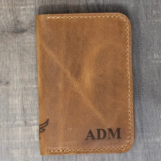 Tan leather bifold wallet with the initials ADM engraved in serif capitals in the lower right corner