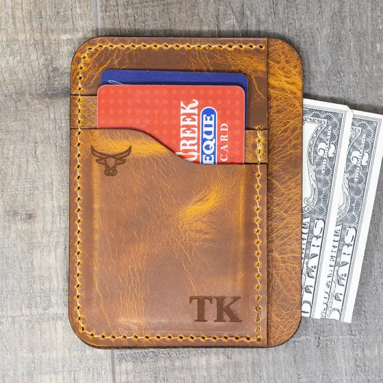Tan front-pocket card wallet with the initials TK engraved in the lower right corner, cards and cash showing
