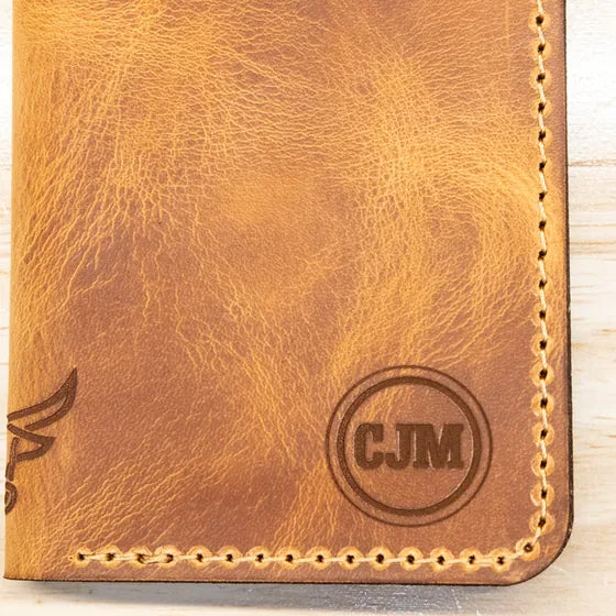 Tan leather wallet with the initials CJM engraved inside a circle monogram near the lower right corner