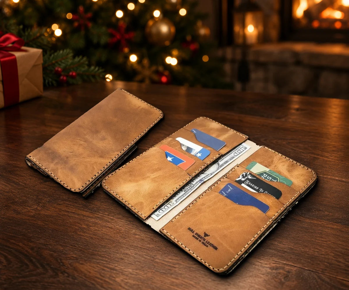 The Houstonian Long Wallet in Saddle Tan, open with cards and cash and shown closed, on a table by a lit Christmas tree