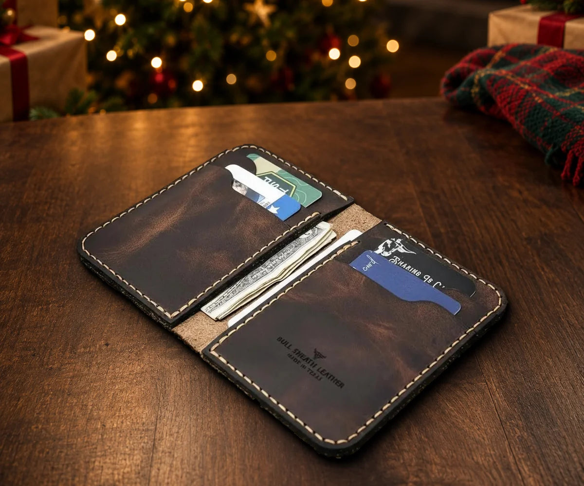 The Tyler Vertical Wallet in Walnut Brown, open with cards and cash, on a table by a lit Christmas tree