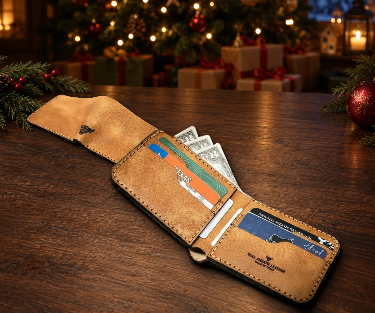 The Rio Grande Bifold Wallet in Saddle Tan, open with cards and cash and shown from the outside, on a table by a lit Christmas tree